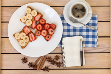 coffee and toast with strawberries and bananas . notepad and pen