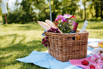 Picnic basket with drinks, food and flowers on the grass