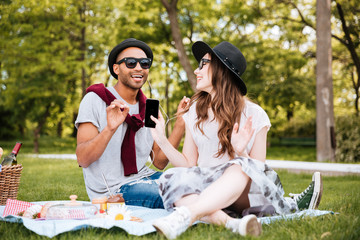 Smiling couple listening to music from cell phone on picnic