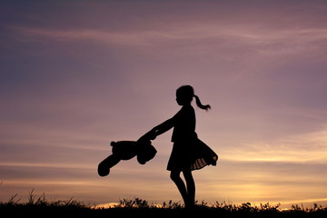 Obraz na płótnie Canvas Silhouette a girl and bag with teddy bear at sky sunset