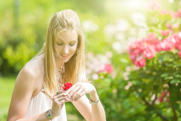 Portrait of beautiful natural young woman holding red rose in the hand in the rose garden