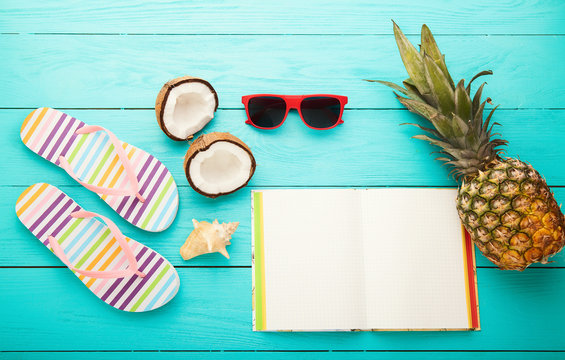 Beach accessories, fruits and notebook on blue wooden background. Top view and copy space