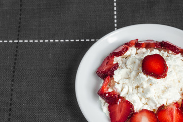 Slices strawberries is lying on delicious cottage cheese. Cottage cheese is lying on a plate with slices of strawberries.
