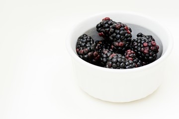 High contrast image of blackberries in a white dish  on a white background.