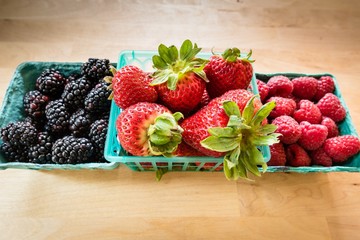 Blackberries, strawberries and red raspberries in green market containers on a wood counter.