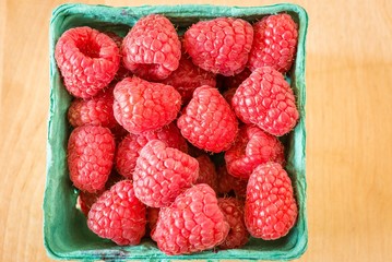Red raspberries in a green market container on a wood counter.