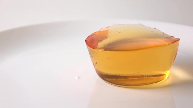Macro super slow motion video of orange jelly falling on white plate
