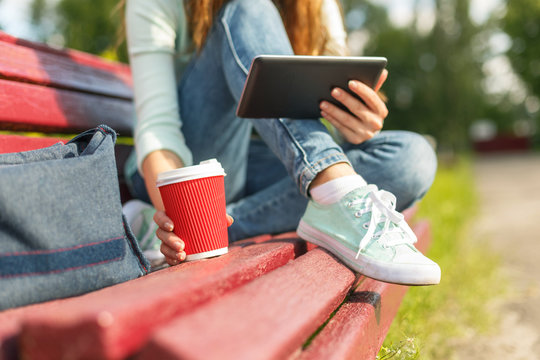 Young Woman With A Coffee To Go And Tablet Pc On A Bench