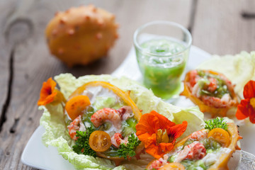 Exotic Shrimp salad served in n half a kiwano and leaves of the Chinese cabbage for summer party on wooden table, selective focus, copy space