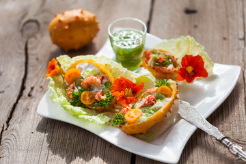 Exotic Shrimp salad served in n half a kiwano and leaves of the Chinese cabbage for summer party on wooden table, selective focus, copy space