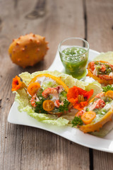 Exotic Shrimp salad served in n half a kiwano and leaves of the Chinese cabbage for summer party on wooden table, selective focus, copy space