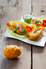 Exotic Shrimp salad served in n half a kiwano and leaves of the Chinese cabbage for summer party on wooden table, selective focus, copy space