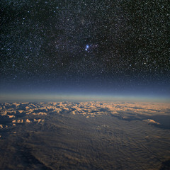 High altitude view of snowy mountains and cloud with stars above.