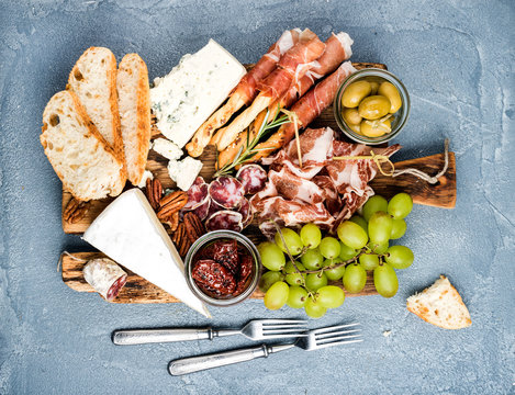 Cheese and meat appetizer selection or wine snack set. Variety of  , salami, prosciutto, bread sticks, baguette, honey, grapes, olives, sun-dried tomatoes, pecan nuts over grey concrete textured