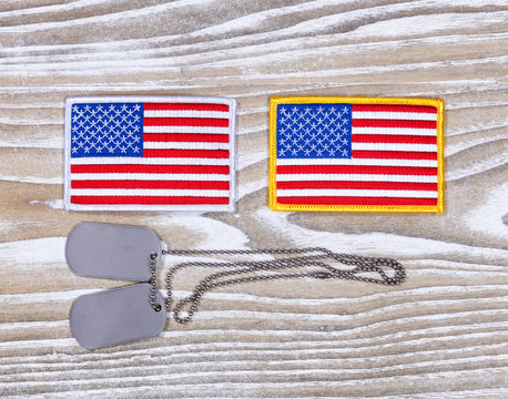 Small USA flag patches and military ID tags on rustic white wood
