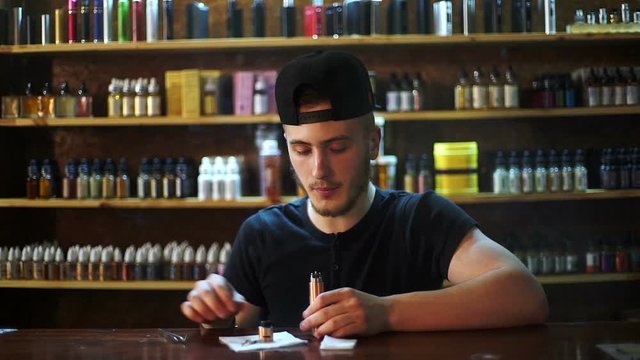 young seller in vape shop is installing cotton in atomizer show window in background