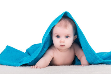 cute baby child with big eyes under blue towel on white, isolated. baby lying on a soft blanket, looking at the camera and tries to crawl on his belly