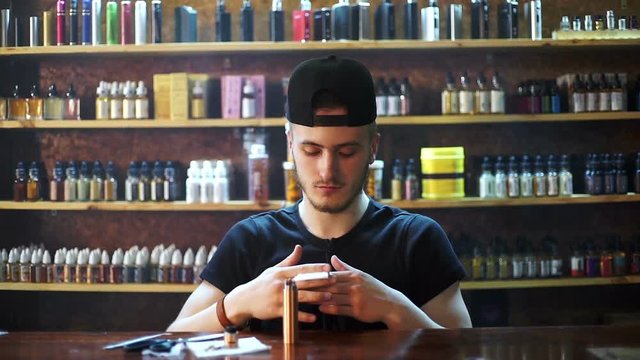 young seller in vape shop is installing cotton in atomizer show window in background