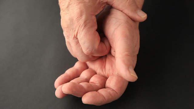 An older man attempts to minimize the involuntary shaking of his thumb.