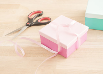 Gift wrapping for a holiday celebration, birthday or surprise party. Preparation of present with ribbon, box and decoration on table. Festive package material.