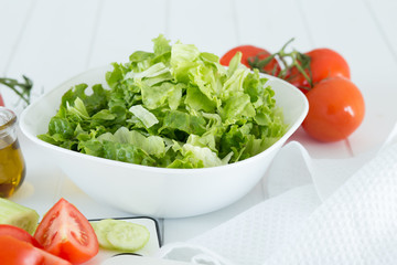 Preparing a healthy fresh salad with tomato, lettuce, cucumber and oil