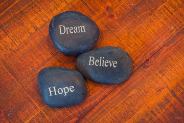 Obraz na płótnie Canvas Black inspirational pebble stones with the words Dream, Believe and Hope on wooden background