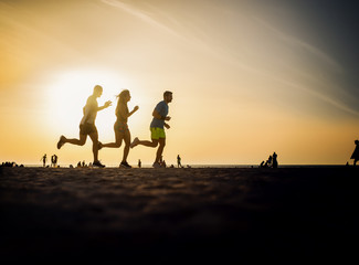 Fitness people running at the beach into the sunset.