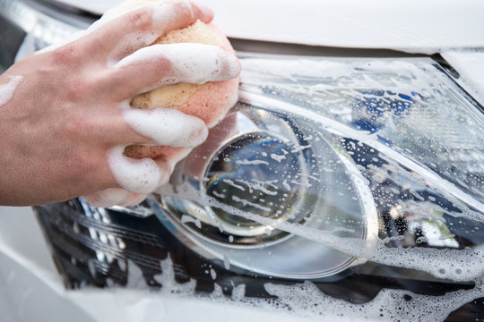 handle carwash concept - man washing car headlamp with sponge an