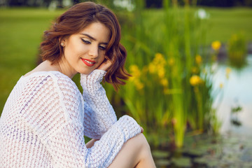 Outdoor photo of young woman near the pond. Beautiful tender woman with red hair posing in summer park.