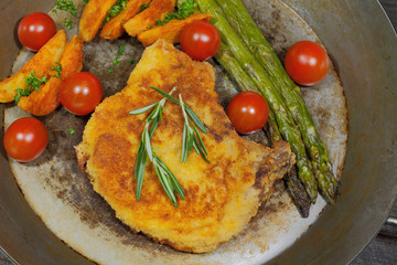 Cutlet with potato wedges, tomatoes, green asparagus, garnished
