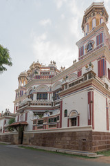 Fototapeta na wymiar Chettinad, India - October 17, 2013: Chidambara Palace in Kadiapatti. Corner view on facade shows towers, balconies, balustrades, the front entrance, Krishna decorations. Mainly beige and purples