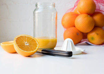 Orange halves with knife, juicer, glass jar and bag of oranges on white table (selective focus)