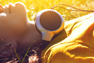 pretty girl lying in summer grass with headphones listening to m