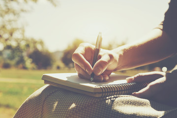 girls hands with pen writing on notebook in park - 113575494