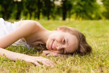 Obraz na płótnie Canvas Portrait of a beautiful young girl lying on the grass outdoors in summer