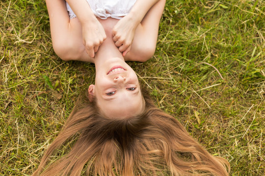 Portrait of a beautiful young girl lying on the grass outdoors in summer