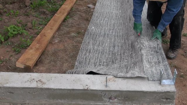 Worker cutting ruberoid for waterproofing cement foundation with knife