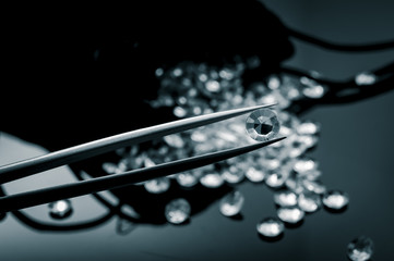 Monochrome image of a jeweler inspecting with tweezers one diamond of the many diamonds in a pile...