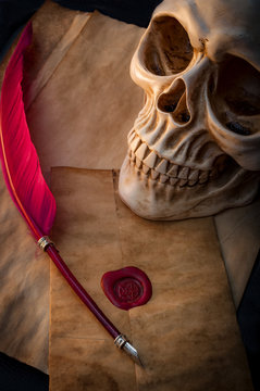 Candle lit scene of a skull, aged paper with a pentagram wax seal on it and a red feather fountain pen