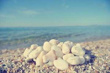 Heap of white pebbles on the beach, on a sunny day, with blue sea in the background. Image filtered in faded, washed-out, retro, Instagram style; nostalgic concept of summer holidays. - 113583051