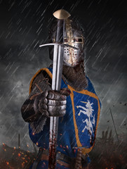 A knight with sword under the rain on battlefield.