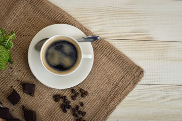 Cup of hot fragrant coffee with beans and chocolate on a mesh fabric.
