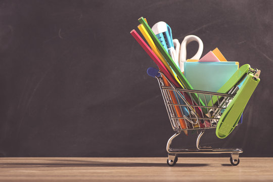 Shopping cart with school supplies over chalkboard background