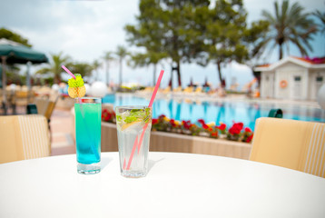 Cocktail mojito and other bright cocktail on a table in the hotel restaurant or on the background of palm trees and a swimming pool sunny summer day
