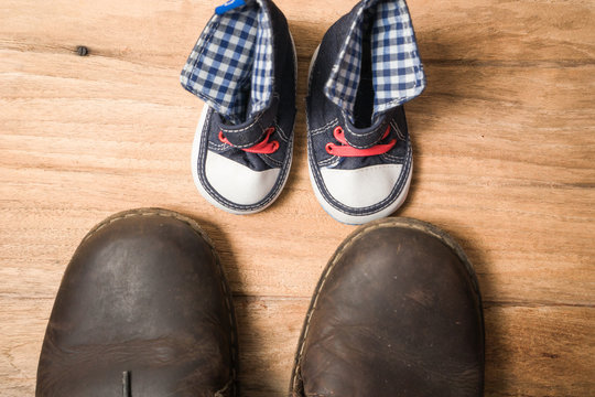 Daddy's boots and baby's sneakers, on wood background, fathers d