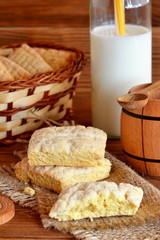 Delicious home cookies on a burlap. A bunch of biscuits in a basket. Cow's milk in a glass bottle. Small decorative barrel and spoon. Wooden table. Rustic style. Vertical photo. Closeup