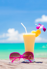 fresh exotic banana and pineapple cocktail and sunglassses on a wooden table by the beach