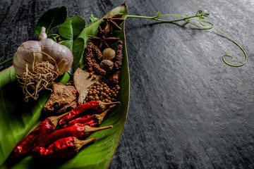 Herbs and spices around empty cutting board on dark stone backgr
