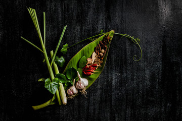 Herbs and spices around empty cutting board on dark stone backgr
