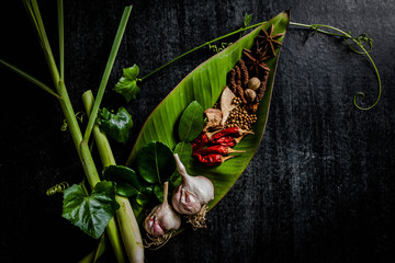 Herbs and spices around empty cutting board on dark stone backgr